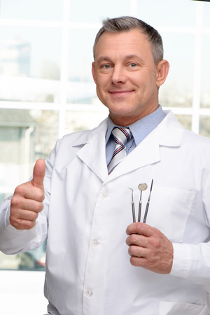 Photo of dentist holding stomatologist tools and showing thumb up. Concept for teeth hygieneの写真素材