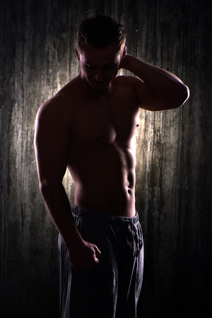 Silhouette photo of young handsome well formed sporty man. Man demonstrating muscles with his arm raised up. Fitness conceptの写真素材