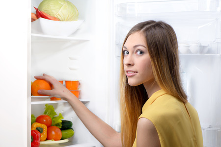 Young beautiful woman looking at camera and picking food from fridge.の写真素材