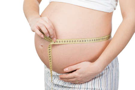 Close up photo of young pregnant woman belly. Woman measuring belly with yellow tape. Isolated on white background. Concept for pregnancyの写真素材
