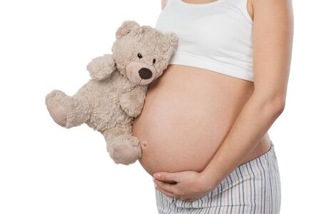 Close up photo of young pregnant woman belly. Woman holding teddy bear near her belly. Isolated on white background. Concept for pregnancyの写真素材