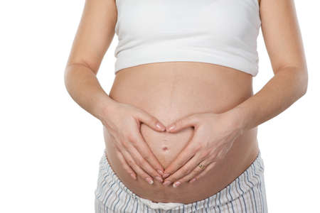 Close up photo of young pregnant woman belly. Woman making hand heart on her belly. Isolated on white background. Concept for pregnancyの写真素材