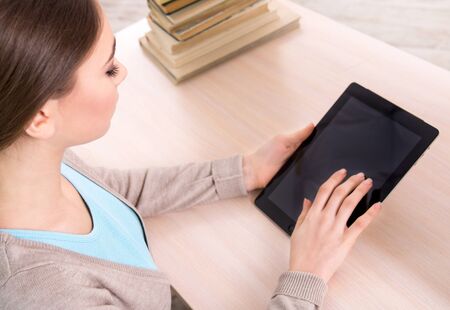 Top view photo of girl working with tablet computer and sitting near stack of books. Concept for teenagersの写真素材