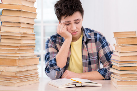 Nice photo of unhappy boy wearing plaid shirt. He reading book and sitting near stacks of books. Concept for teenagersの写真素材
