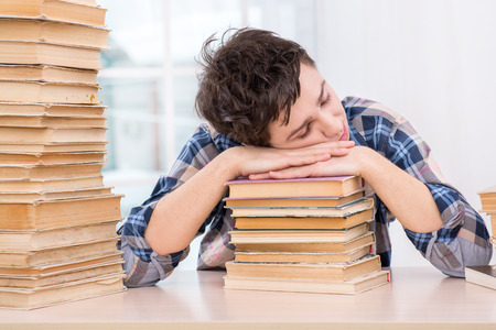 Nice photo of sleeping boy on books. Boy sitting in light room with large window near stack of books. Concept for teenagersの写真素材