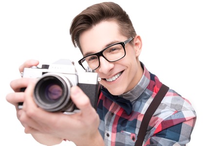 Young nerd in glasses and checkered shirt with retro camera isolated on white backgroundの写真素材