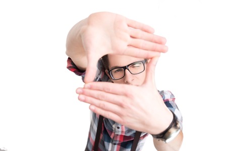 Young nerd in glasses and checkered shirt making picture frame by hands isolated on white backgroundの写真素材
