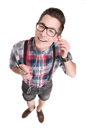 Young nerd in glasses and checkered shirt listening to music with smartphone isolated on white backgroundの写真素材