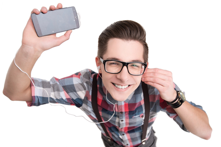 Young nerd in glasses and checkered shirt listening to music with smartphone isolated on white backgroundの写真素材