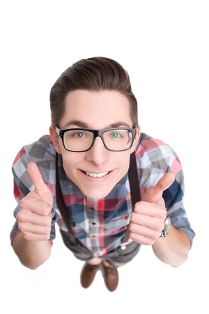 Young nerd in glasses and checkered shirt gesturing thumbs up isolated on white backgroundの写真素材
