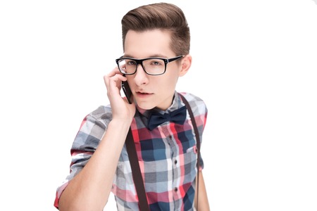 Young nerd in glasses and checkered shirt with smartphone isolated on white backgroundの写真素材