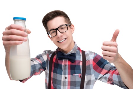Young nerd in glasses and checkered shirt with bottle of milk gesturing thumb up isolated on white backgroundの写真素材