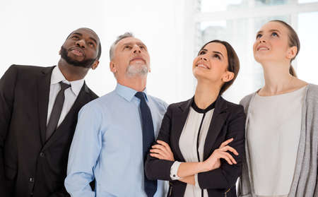 Multi-ethnic business team standing in office, smiling and looking upの写真素材