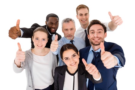 Multi-ethnic business team standing isolated on white, looking up, smiling and showing thumbs up to cameraの写真素材