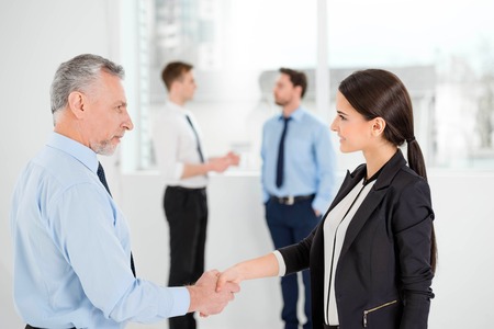 Aged businessman and young businesswoman shaking hands. Business people communicating in the backgroundの写真素材