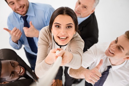 Top view of young smiling businesswoman reaching up along rope. Other members of business team cheering her up. Isolated on white backgroundの写真素材