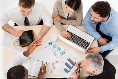 Top view of business team discussing project. There are graphs, laptop and tablet computer on tableの写真素材