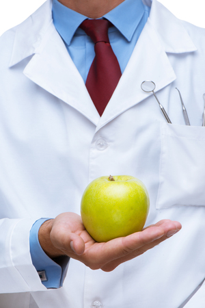 Close up photo of dentist. There are dental instruments and toothbrush in his pocket. He holding green apple. Vertical photoの写真素材