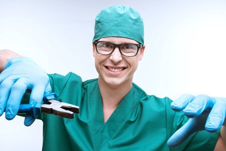 Funny photo of terrible dentist. He holding pliers, smiling frighteningly and looking at cameraの写真素材