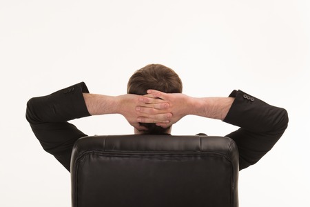 Back photo of young businessman wearing suit and holding hands behind head. Isolated on white backgroundの写真素材