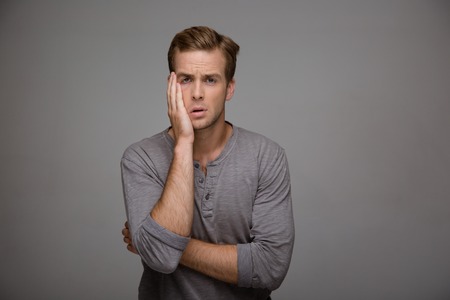 Portrait of handsome stylish young man on grey background. Sad and tired man looking at cameraの写真素材
