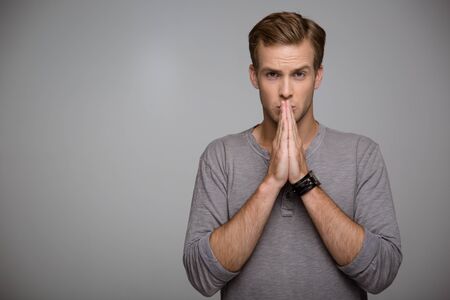 Portrait of handsome stylish young man on grey background. Self-confident man looking at camera and prayingの写真素材