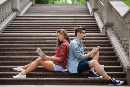 Portrait of beautiful young woman and handsome man on vacation. Girl and boy sitting back to back on marble staircaseの写真素材