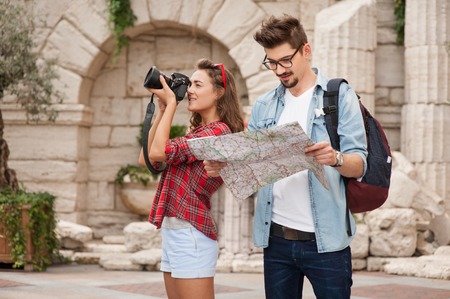 Portrait of beautiful young woman and handsome man on vacation. Girl making photo on camera. Boy studying mapの写真素材