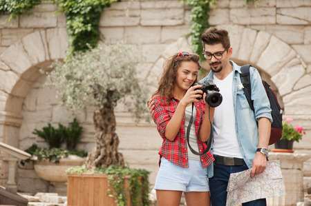 Portrait of beautiful young woman and handsome man on vacation. Girl and boy viewing photos on cameraの写真素材