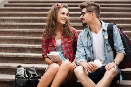 Portrait of beautiful young woman and handsome man on vacation. Girl and boy looking at each other, smiling and sitting on marble staircaseの写真素材