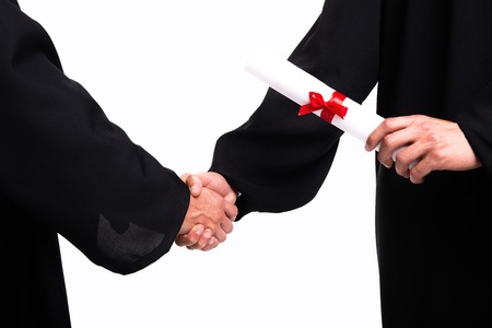 Close up photo of two young student boys dressed in black graduation gown. Isolated on white background. Boys shaking handsの写真素材