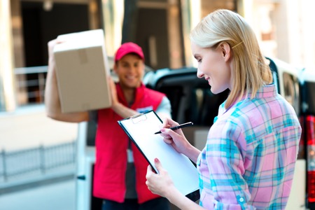 Colorful picture of courier delivers package for woman. Woman is receiving the parcel and smiling.の写真素材