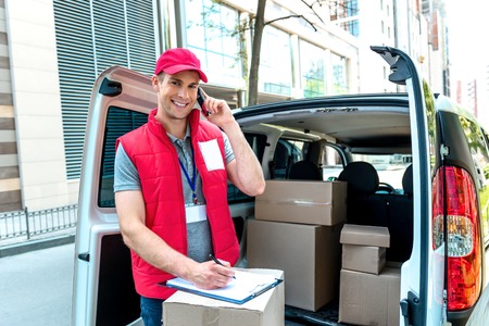 Colorful picture of courier delivers package. Courier talking on the phone, looking at camera and smiling.の写真素材