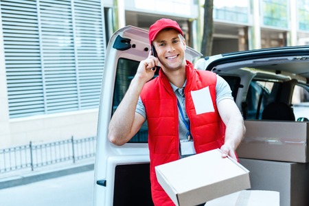 Colorful picture of courier delivers package. Courier talking on the phone, giving the parcel and smiling.の写真素材