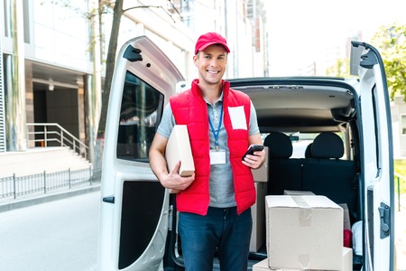 Colorful picture of courier delivers package. Courier holding the box and phone, he smiling.の写真素材