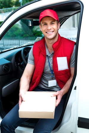 Colorful picture of courier delivers package. Man is sitting in the car, holding the box and smiling.の写真素材