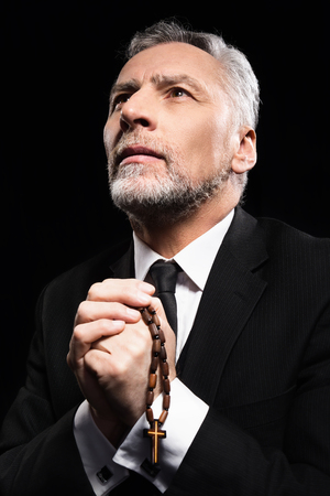 Photo of old man praying to God with rosary on black backgroundの写真素材