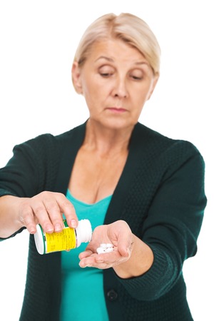 Portrait of senior blonde woman standing isolated on white background. Unhappy woman looking at pills at her handの写真素材
