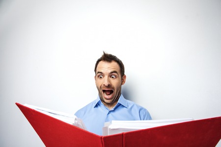 Funny photo of businessman with beard wearing shirt. Surprised businessman looking at folder full of documents with eyes wide open. Isolated on white backgroundの写真素材