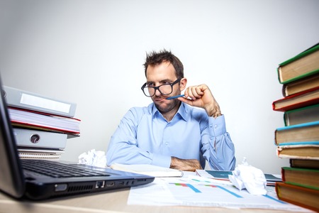 Funny photo of businessman with beard wearing shirt and glasses. Overworked businessman working with laptop at table full of documents. Isolated on white backgroundの写真素材