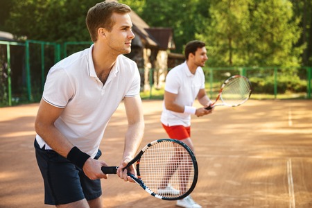 Picture of handsome young men on tennis court. Men playing tennis. Man is ready to hit tennis ball. Beautiful forest area as backgroundの写真素材