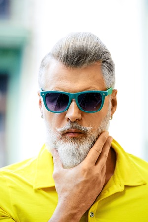 Portrait of stylish handsome adult man with beard standing outdoors. Man wearing glasses and yellow T-shirt, and looking at cameraの写真素材