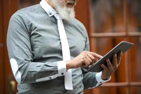 Close up of stylish handsome adult man with beard standing outdoors. Man using tablet computerの写真素材