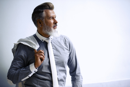 Portrait of stylish handsome adult man with beard standing outdoors. Man wearing tie and holding jacketの写真素材