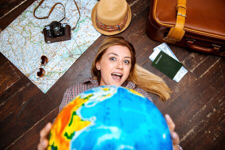 Top view photo of beautiful blonde girl lying on wooden floor. Young woman smiling and showing globe...
