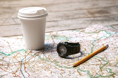 Photo of world map, white cup of coffee, pencil and watch. Objects are on light colored wooden floor
