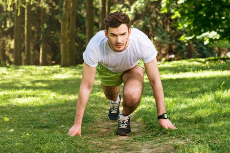 Photo of handsome nice guy outdoors at morning. Young man looking at camera and ready to race while...