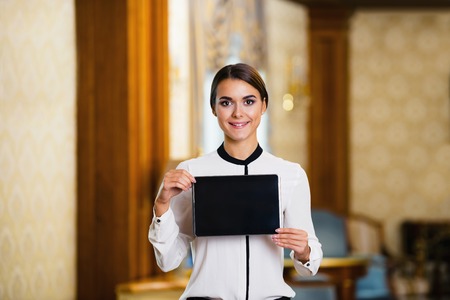 Young business woman standing in nice hotel room, holding tablet computer and looking at cameraの写真素材