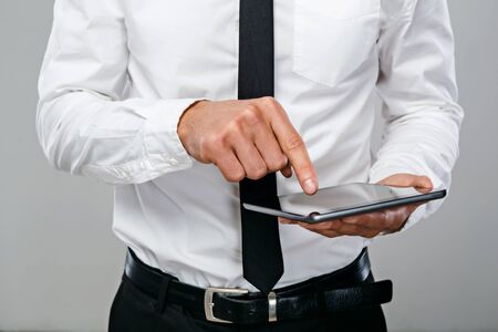 Close up photo of young businessman standing on grey background wearing shirt and tie and using tablet computerの写真素材