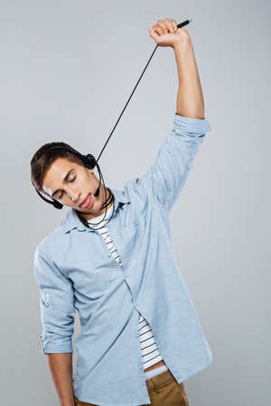 Portrait of handsome stylish young male call center operator standing on grey background pretending that hanging on wireの写真素材